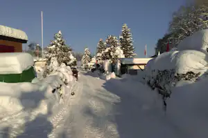 Verschneiter Campingplatz mit Zelten und Wohnwagen, schneebedeckten Bäumen und einem Weg zwischen den Unterkünften.