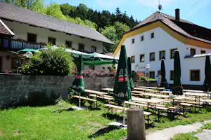 Campinganlage mit zwei Ferienhäusern, Terrasse und Garten, Holztischen und Stühlen sowie grünen Markisen vor bewaldetem Hang.