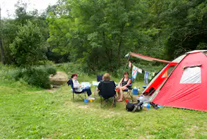 Rotes Zelt auf einer Wiese, daneben Campingstühle und ein Tisch mit Getränken, im Hintergrund Bäume und ein weiteres Zelt.