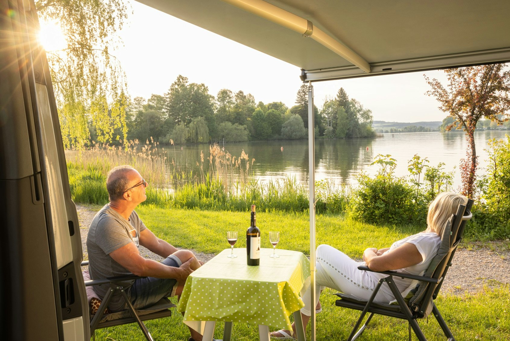 Camping Schwanenplatz - Camper sitzen gemeinsam auf ihrem Standplatz mit Blick auf den See