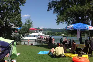 Camping Seeblick - Camper im Schatten auf einer Wiese am See vom Campingplatz