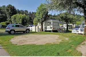 Wohnwagen und Zelte auf einem Campingplatz, mit geparkten Autos, Rasenfläche und Bäumen im Hintergrund.