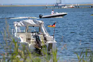Boot am Ufer im See, im Hintergrund ein Steg und ein weiteres Boot mit Personen.