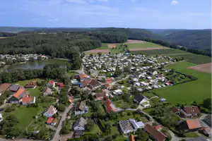 Luftaufnahme eines Campingplatzes mit vielen Wohnwagen und Zelten, umgeben von Wiesen, Feldern und Waldhängen.