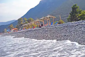 Schotterstrand mit Zelten am Ufer, im Hintergrund Berge und bewaldete Hänge.