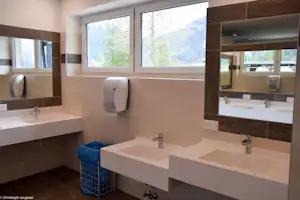 Modernes Camping-Badezimmer mit zwei Waschbecken, Spiegeln und großen Fenstern mit Blick auf Berge und Bäume.
