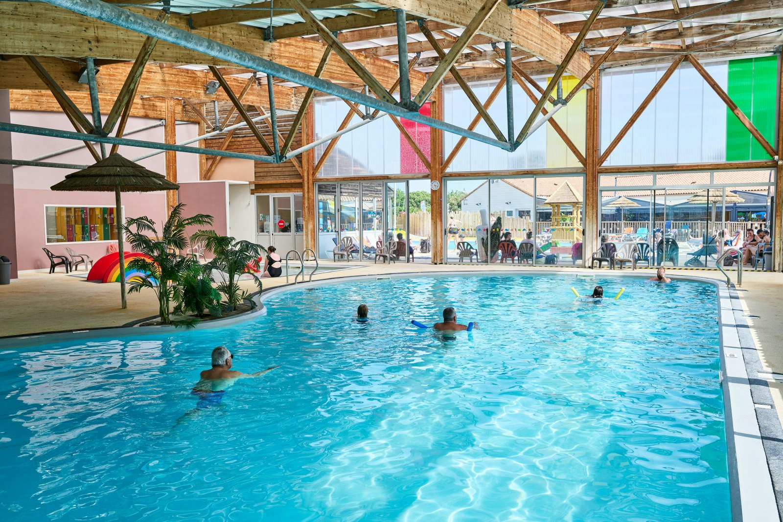 Innenpool im Campingbereich mit blauem Wasser, Holz-Dachkonstruktion und Liegen am Beckenrand.