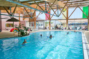 Innenpool im Campingbereich mit blauem Wasser, Holz-Dachkonstruktion und Liegen am Beckenrand.