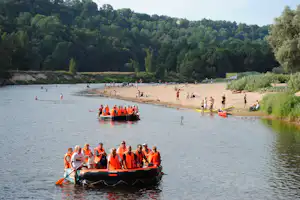 Boot mit Rettungswesten auf dem Fluss vor einem Sandstrand mit vielen Badegästen und Rafting-Gummibooten.
