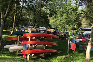 Rote Kanus auf Holzgestellen im Schatten von Bäumen, im Hintergrund weitere Boote und Wohnwagen auf dem Campingplatz.
