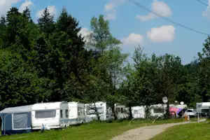 Wohnwagen und Zelte auf einem grünen Campingplatz, mit Kiesweg und Bäumen im Hintergrund.