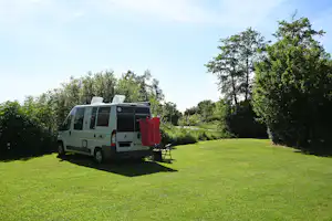 Wohnmobil auf grünem Campingplatz mit geöffnetem Vorzelt, Tisch und Stühlen auf dem Rasen, umgeben von Bäumen.