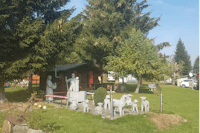 Camping Sinntal - Brunnen und Tierstatuen vor einem Mobilheim unter Bäumen auf dem Campingplatz
