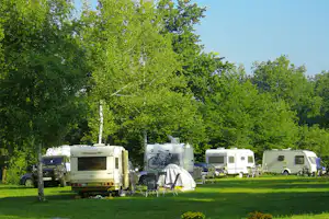 Wohnmobile auf einem Campingplatz im Grünen, mit Stühlen und Tisch vor dem Zelt, umgeben von Bäumen.