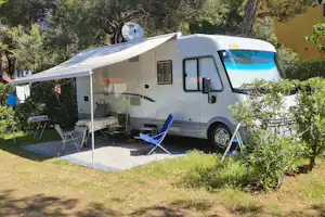 Wohnmobil mit Vorzelt und Sitzbereich auf einem Campingplatz im Grünen, umgeben von Bäumen und Rasen.