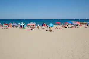Sandstrand mit vielen Sonnenschirmen und Strandzelten, Menschen liegen am Ufer, im Hintergrund das Meer.
