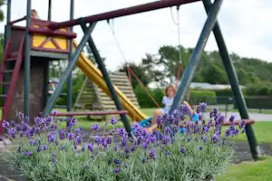 Spielplatz mit Rutsche und Klettergerüst, im Vordergrund Lavendelblüten und ein Kind auf dem Spielbereich.