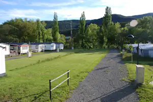 Reihen von Wohnwagen und Mobilheimen auf einem Campingplatz, mit gepflegtem Rasen, Kiesweg und Bäumen im Hintergrund.