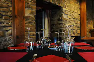Tisch mit roter Tischdecke und Gläsern im Restaurantbereich mit Steinwand und Holzsäulen.