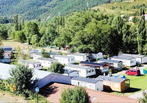 Campinganlage mit Wohnmobilen und Mobilheimen, umgeben von Wald und Hügeln, mit rotem Auto auf dem Stellplatz.