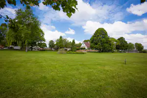 Weite Rasenfläche auf dem Campingplatz mit Bäumen, Gartenwegen und mehreren Gebäuden im Hintergrund.