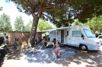 Camping & Spa CAP SOLEIL  -  Camper Familie am Wohnmobil auf dem Stellplatz vom Campingplatz im Schatten eines Baumes