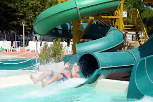 Grüne Wasserrutsche mit Rutschenturm, Kinder im Becken und Spritzwasser im Vordergrund.