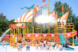 Bunte Wasserrutsche mit Sprühfontäne und Kinderbereich, viele Kinder stehen im Becken vor dem Rutschenturm.