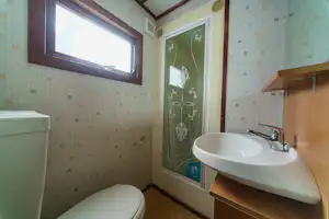 Bad mit Waschbecken, Armatur und Fenster, gefliest mit kleinen Mustern; daneben Toilette und Handtuchhalter.
