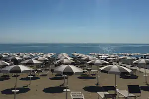 Reihe von Strandliegen unter weißen Sonnenschirmen am Campingplatz, Blick aufs Meer und den Horizont.