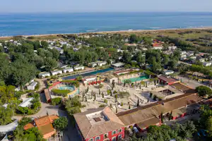 Luftaufnahme eines Campingplatzes mit Schwimmbecken, Stellplätzen, Wegen und Bungalows, umgeben von Bäumen und nahe dem Meer.