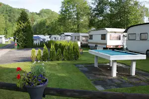 Wohnwagen auf einem Campingplatz, gepflasterter Weg und Rasen mit Tisch vor weiteren Stellplätzen und Bäumen.