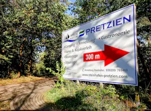 Wegweiser am Campingplatz mit Aufschrift Steinhafen, Camping und Anmeldung, 300 m, Bootssteg und Slipanlage vor Wald und Weg.