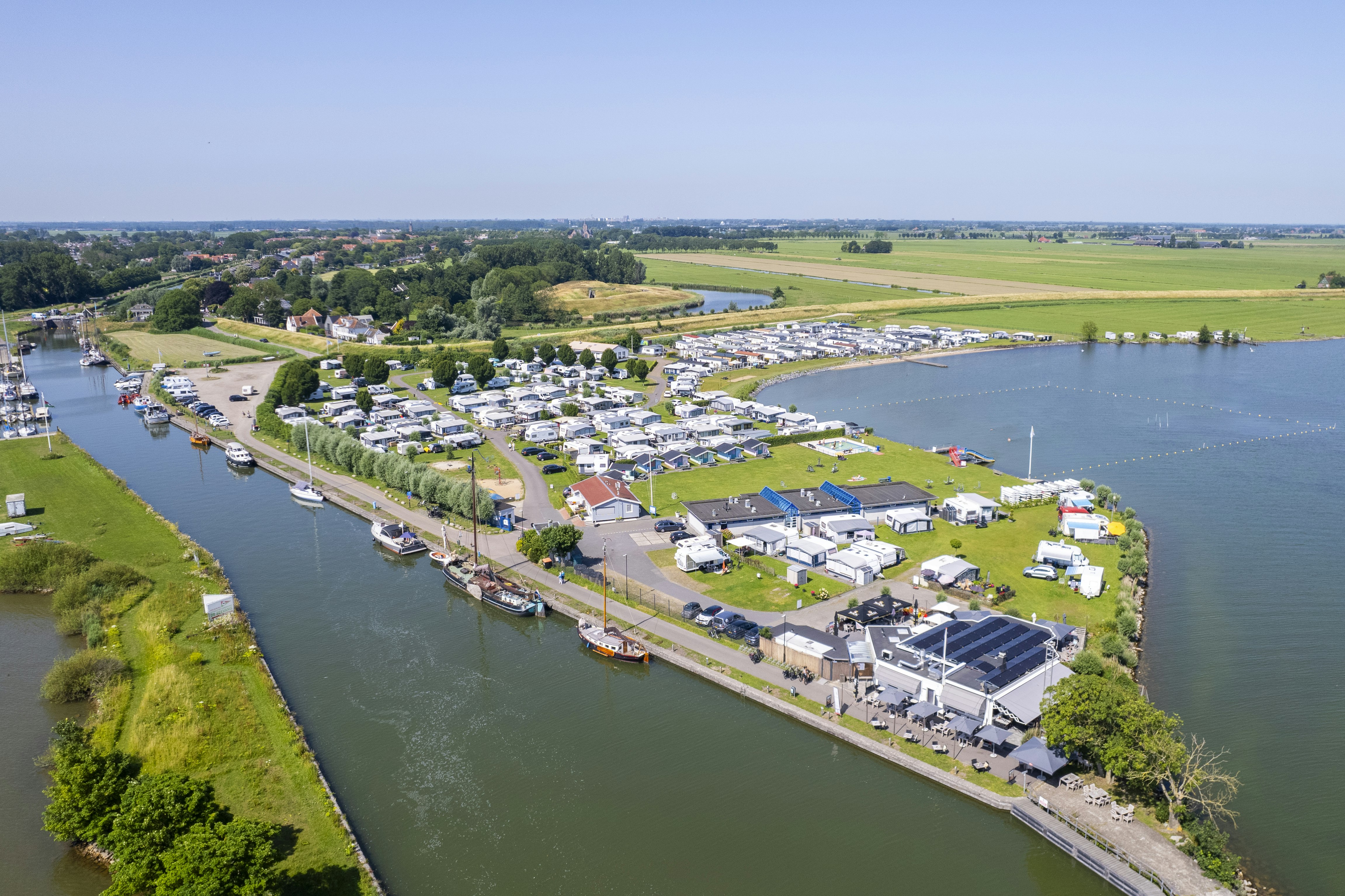 Luftaufnahme eines Campingplatzes am Fluss mit vielen Stellplätzen und Wohnwagen, Stegen und Grünflächen am Ufer.