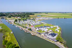 Luftaufnahme eines Campingplatzes am Fluss mit vielen Stellplätzen und Wohnwagen, Stegen und Grünflächen am Ufer.