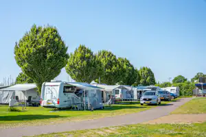 Reihe von Wohnmobilen und Wohnwagen auf einem Campingplatz, mit Vorzelten, Rasenflächen und einem breiten Weg zwischen den Stellplätzen.