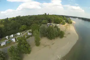 Campingplatz am Fluss mit Sandstrand, Wohnwagen-Stellplätzen, Bäumen und einem Gebäude am Ufer.