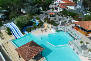 Großes Schwimmbecken mit Sonnendeck, daneben ein kleiner Pool und Liegen, im Hintergrund Gebäude und Bäume.