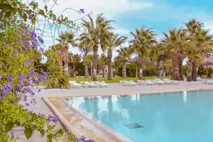 Camping-Pool mit Palmen und lila Blüten, Liegen am Beckenrand und gepflegtem Rasen im Hintergrund.