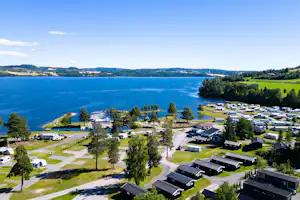 Luftaufnahme eines Campingplatzes am See mit Stellplätzen für Wohnmobile, Gebäuden, Wegen und Bäumen am Ufer.