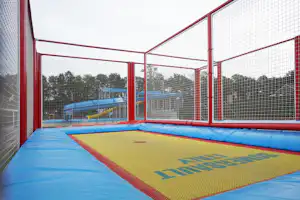 Trampolin-Spielbereich im Camping: blaues Sprungfeld mit Umrandung, gelbe Matte und rotes Netz an den Seiten.