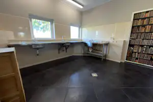 Gemeinschaftsbad im Campingbereich mit mehreren Waschbecken, Spiegeln, Fliesenboden und Handtuchhalter, daneben ein Bücherregal.