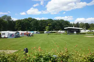 Campingwiese mit Wohnwagen und Zelten, gepflegten Wegen und Bäumen im Hintergrund, daneben ein Gebäude.