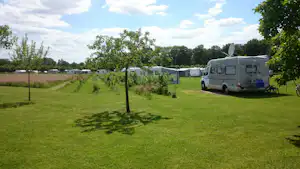 Wohnwagen und Wohnmobil auf einem grünen Campingplatz, mit Rasenwegen, jungen Bäumen und weiteren Stellplätzen in der Ferne.