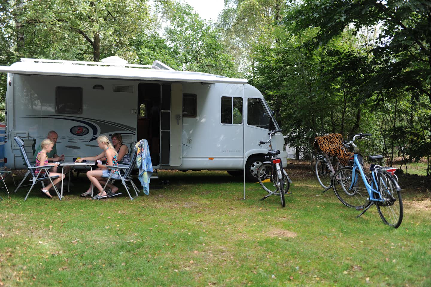 Camping 't Schinkel - Camper sitzen vor dem Wohnmobil im Schatten mit Zeltdach