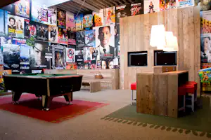 Spielbereich mit Kino-Plakaten an der Wand, Holztresen mit zwei Fernsehern und Tischkicker auf Teppichboden.