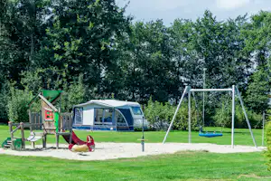 Campingzelt auf dem Rasen, daneben Schaukel und Sandkasten, Holzterrasse mit grünem Sichtschutz im Hintergrund.