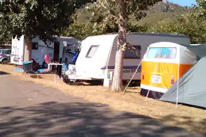 Wohnwagen und Zelt auf einem Campingplatz, mit Baum im Vordergrund und weiteren Fahrzeugen im Hintergrund.