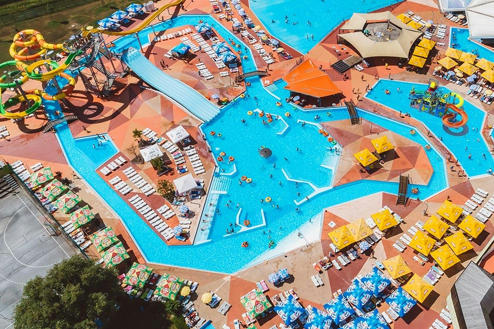 Großer Camping-Schwimmbereich mit mehreren Pools, Rutschen, Liegen und Sonnenschirmen, umgeben von Stellplätzen und Wegen.