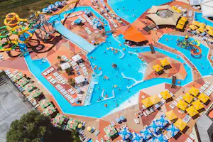 Großer Camping-Schwimmbereich mit mehreren Pools, Rutschen, Liegen und Sonnenschirmen, umgeben von Stellplätzen und Wegen.